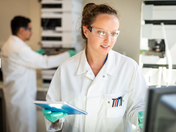 A woman wearing a white lab coat and safety goggles