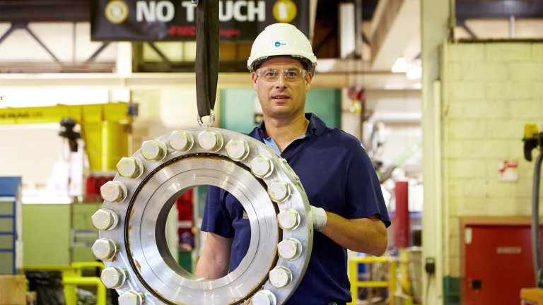 Un employé de T.EN Loading Systems se tient devant une pièce détachée de bras de chargement en métal. arm spare part.