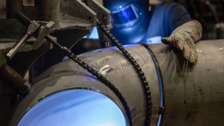 Worker with protective gear welding a metal pipe