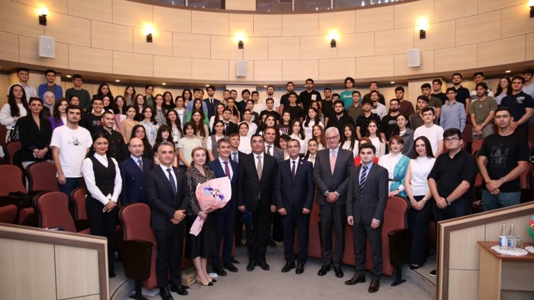 A large group photo of students and officials gathered in an auditorium, smiling and posing together
