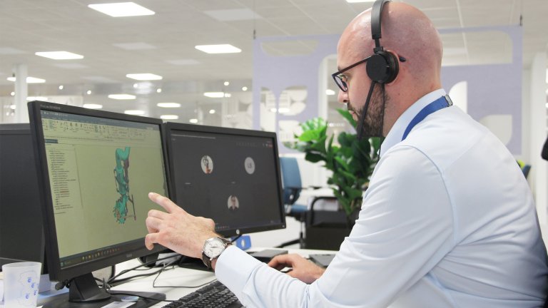 A man working on a computer. He looks at a 3D model while in a call with colleagues