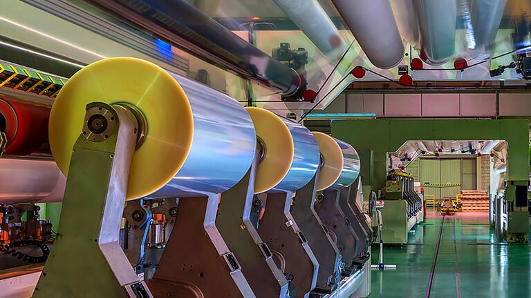A series of large, shiny rolls of tape on a production line in a modern factory