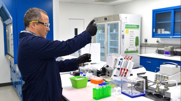 A researcher in a lab coat and safety goggles conducts an experiment with lab equipment, focusing on precise measurements in a modern lab