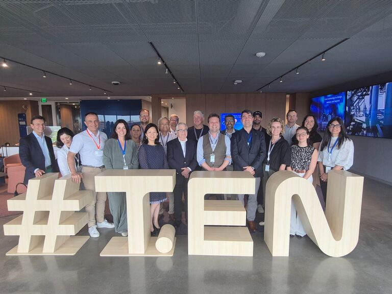 Group photo of professionals standing behind large wooden “#TEN” in a modern office 