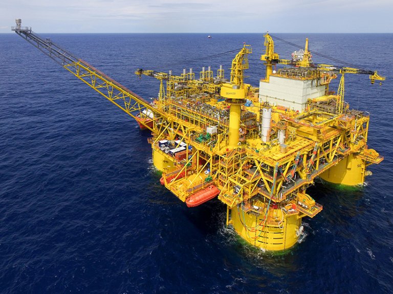 Aerial view of a large yellow offshore oil rig in the ocean, showcasing its structure and equipment