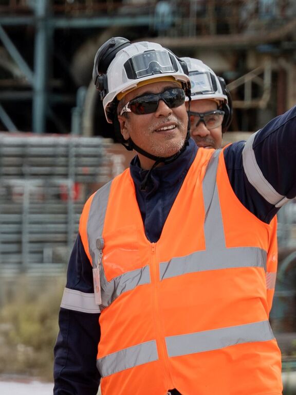 Workers in orange safety vests and hard hats collaborate at an industrial energy site