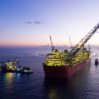 Photo du FLNG Prelude, éclairé par des lumières, et entouré de navires dans des eaux calmes