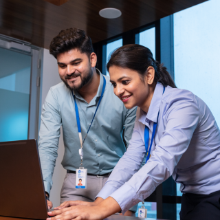 A man and a woman standing in front of a laptop