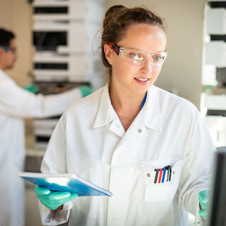 A woman wearing a white lab coat and safety goggles
