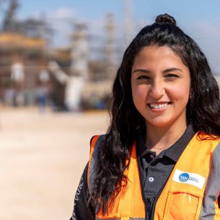 Young woman in an orange safety vest smiles at a construction site