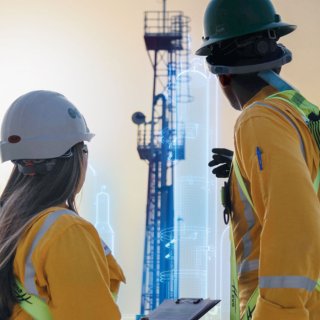 Two engineers in safety helmets observing a tall industrial structure, with digital overlays indicating data analysis