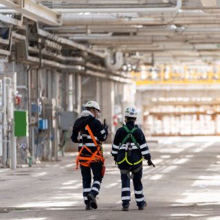 Two workers in safety gear walk through an industrial facility