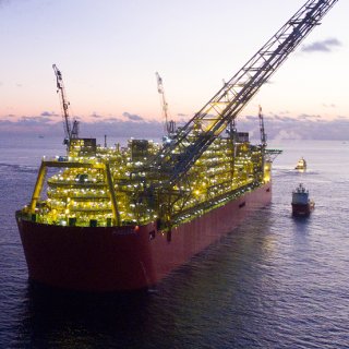 Photo du FLNG Prelude, éclairé par des lumières, et entouré de navires dans des eaux calmes
