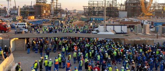 A crowd of workers on a construction site in Egypt, with cranes in the background