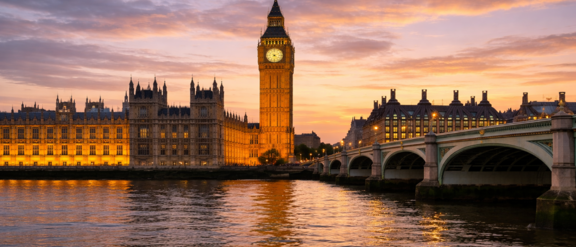 Riverside view of the London clock tower at sunset, with a bridge over the water in the foreground