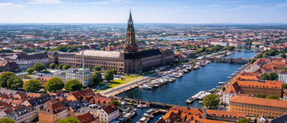Aerial view of Copenhagen with red-roofed buildings, canals lined with boats under a clear blue sky