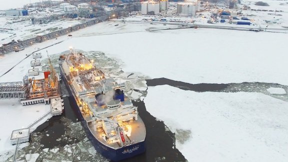 Aerial shot of a ship navigating icy waters near the Yamal industrial complex, in the background