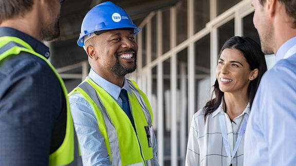 Un groupe de professionnels en gilets de sécurité et en casques discutant d'un projet sur un chantier de construction