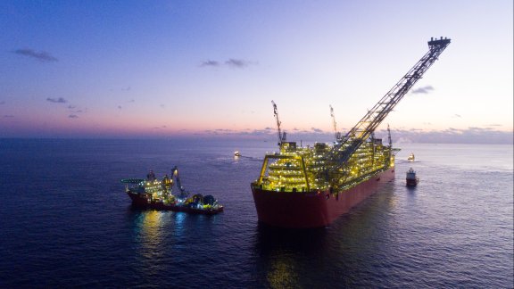 Photo of FLNG Prelude, illuminated with lights, surrounded by vessels in calm waters