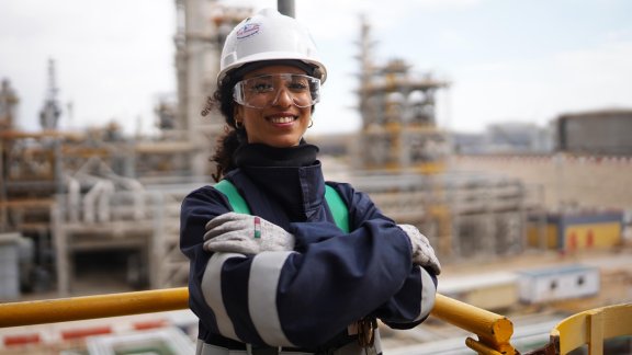 A female engineer in safety gear smiles at a construction site