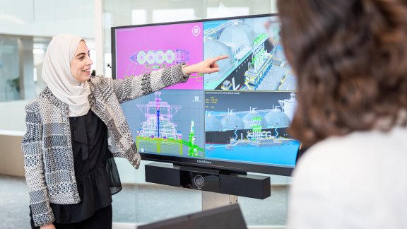 A woman wearing a hijab leading a presentation with 3D mockups on the screen.