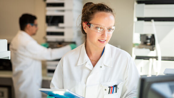 A woman wearing a white lab coat and safety goggles