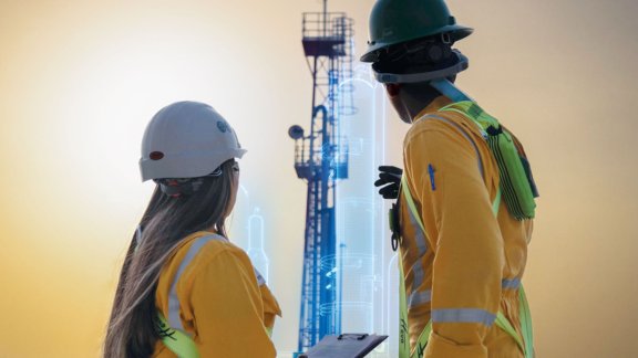 Two engineers in safety helmets observing a tall industrial structure, with digital overlays indicating data analysis
