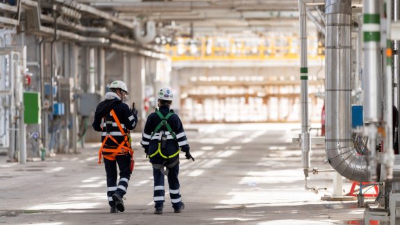 Two workers in safety gear walk through an industrial facility