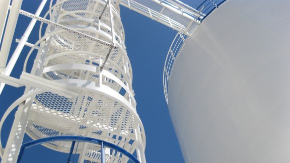 A close-up view of a white industrial staircase leading to a large storage tank