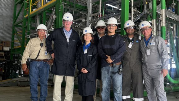 Une équipe de 7 personnes portant des casques avec le logo de Technip Energies sourient et posent pour la photo, avec Wei Cai (Directrice de la Technologie et de l'Innovation) au premier rang