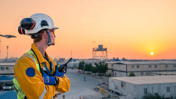 A worker wearing coverall and PPE, looking at the sunrise