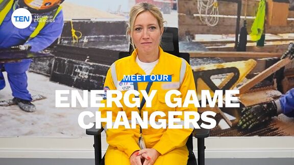 Woman wearing a yellow industrial uniform sitting with a construction backdrop and the text ‘Meet Our Energy Game Changers’ displayed