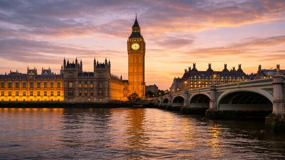 Riverside view of the London clock tower at sunset, with a bridge over the water in the foreground