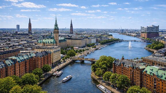 Aerial view of Hamburg with riverside buildings, boats on the water, under a bright sky