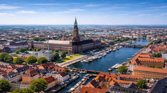 Aerial view of Copenhagen with red-roofed buildings, canals lined with boats under a clear blue sky