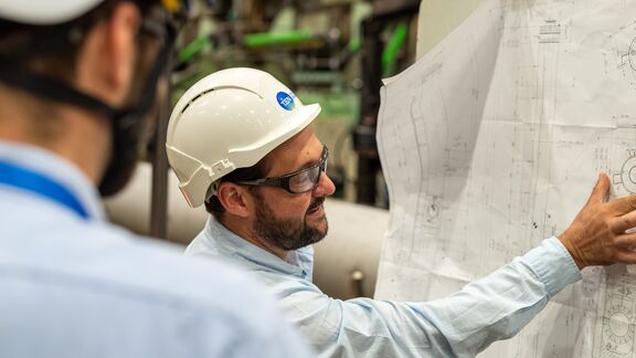 Ingénieur en casque et lunettes de sécurité examinant des plans techniques avec un collègue dans une usine