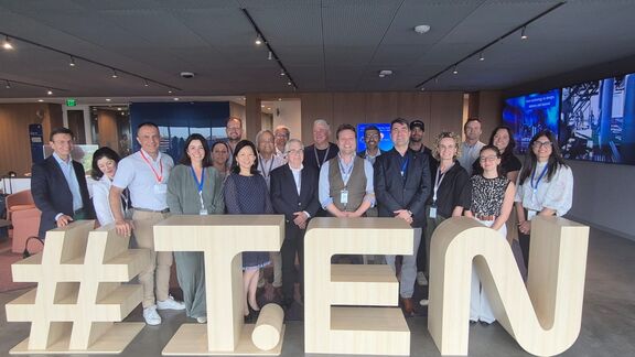 Group photo of professionals standing behind large wooden “#TEN” in a modern office 