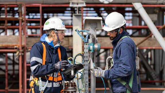 Deux ingénieurs en casque inspectent un équipement électrique industriel dans une centrale, assurant la sécurité et la maintenance