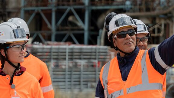 Des travailleurs portant des gilets orange et des casques collaborent sur un site énergétique industriel